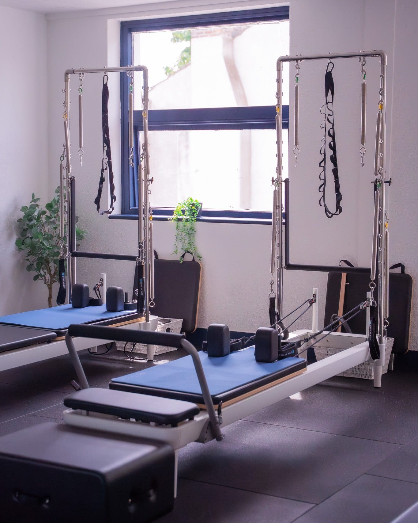 Two reformer machines with tower frames standing beside a window in the studio, springs and straps hanging from the uprights